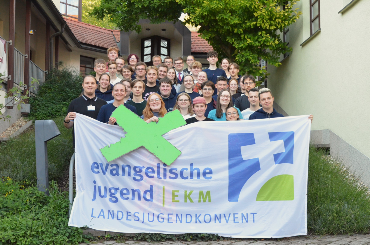 Gruppenfoto LJKHerbstVV2025 Gruppenfoto von etwa 35 jungen Erwachsenen und Jugendlichen, die eng zusammenstehen und fröhlich in die Kamera lächeln. Vorne halten mehrere Personen ein großes Banner mit der Aufschrift ‚evangelische jugend | EKM Landesjugendkonvent‘. © ekmjugend